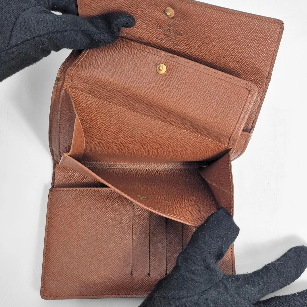 Brown leather wallet held open by a gloved hand on a white background