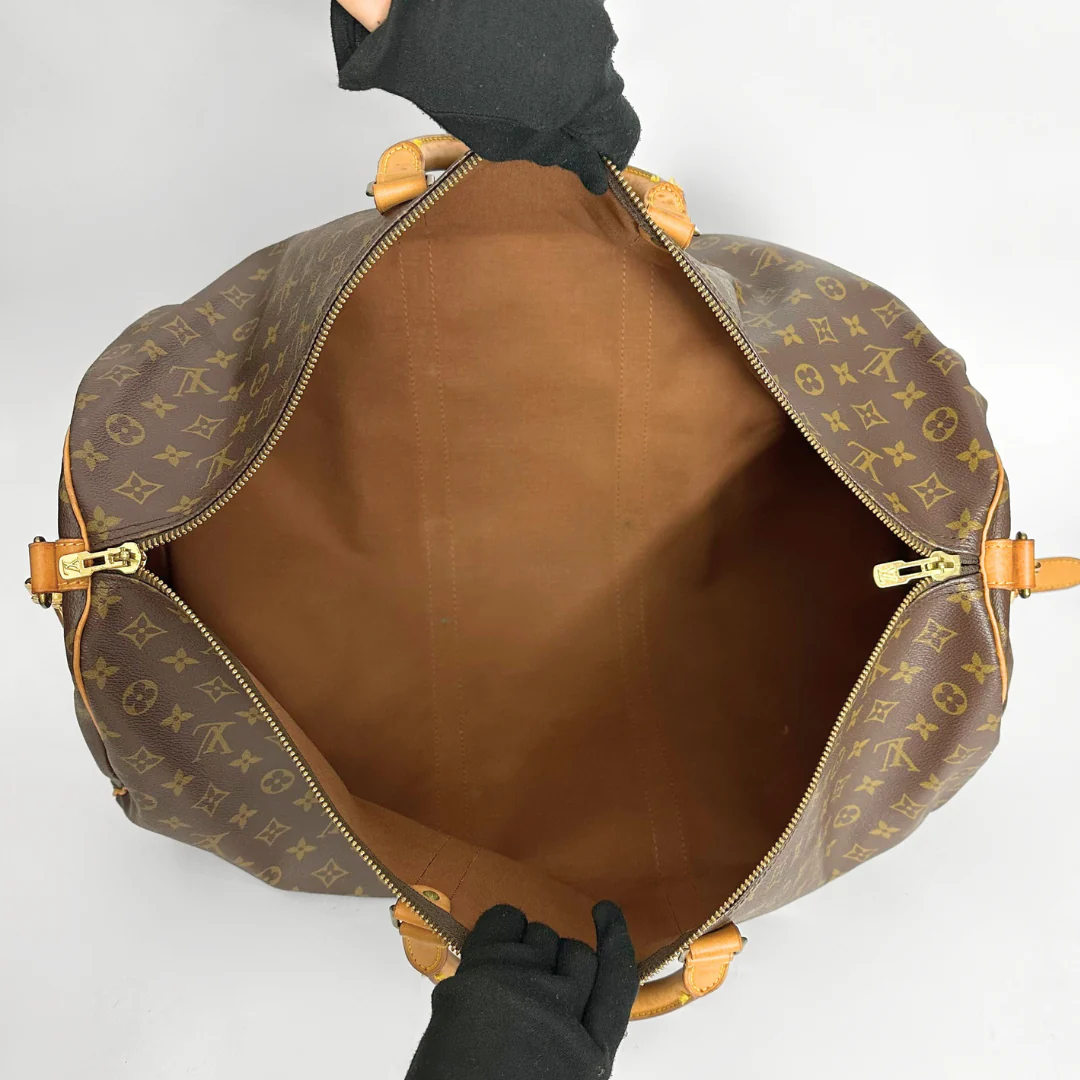 Brown monogrammed bag with gold accents held by a gloved hand on a light gray background
