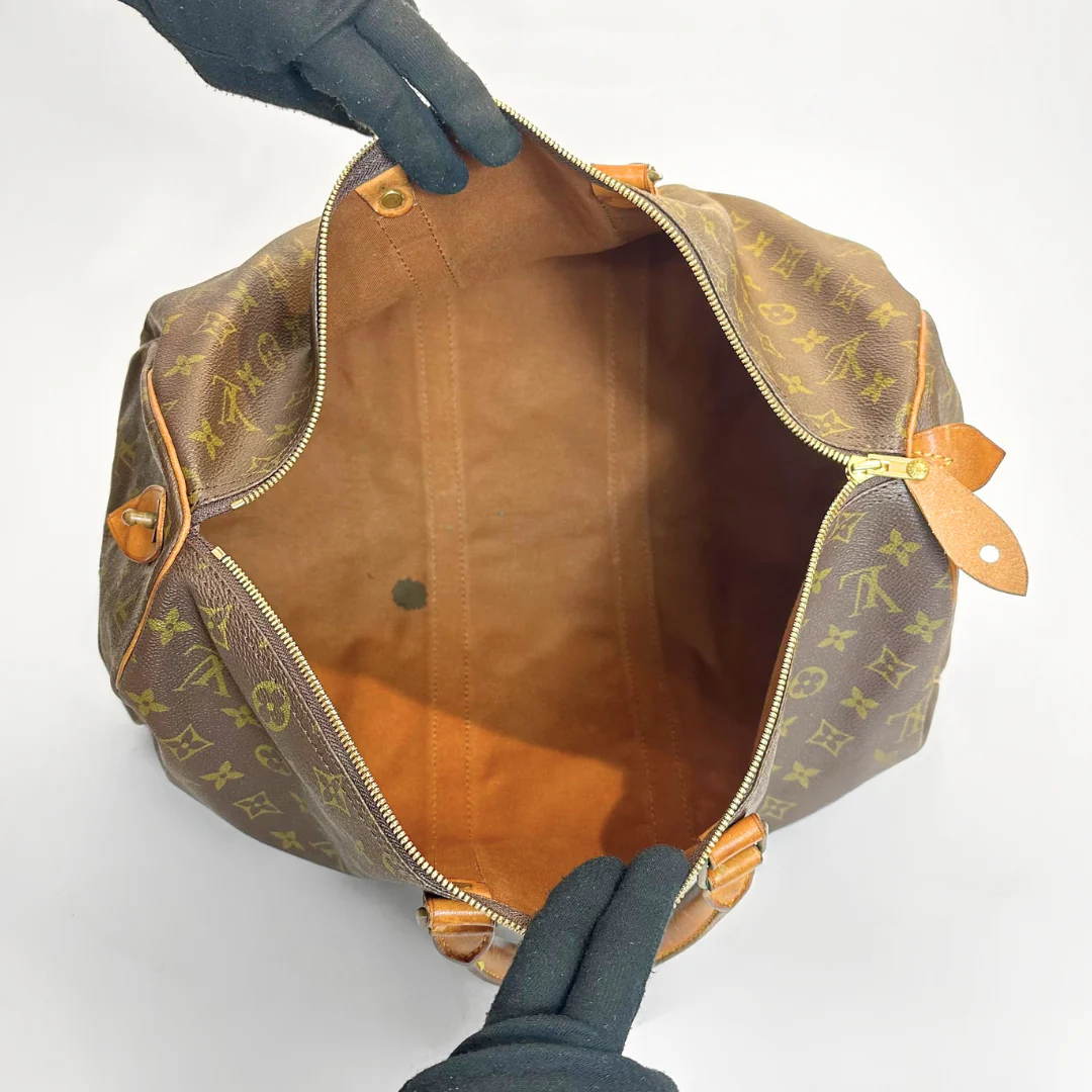 Brown leather bag with monogram pattern held open by a gloved hand on a white background
