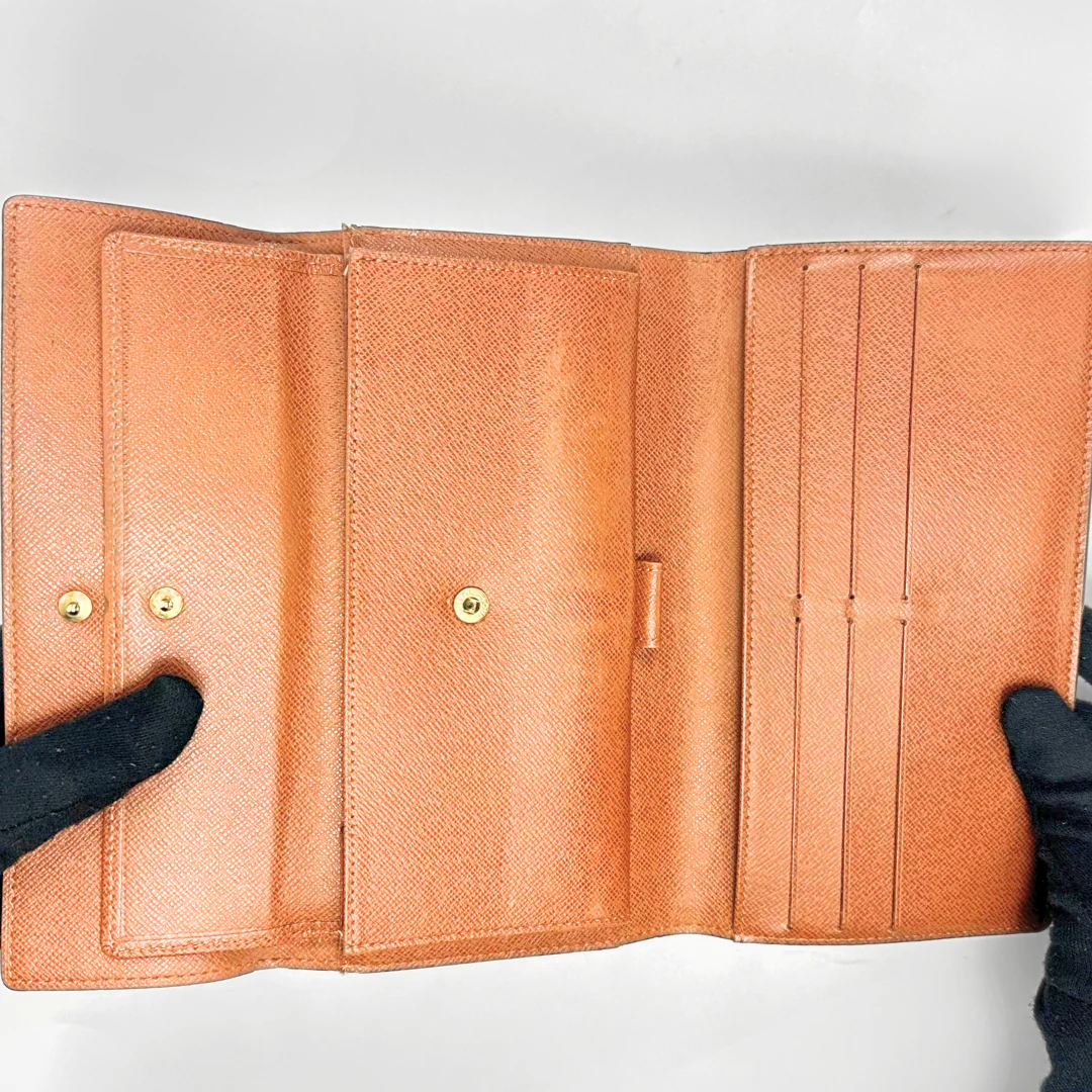 Brown leather wallet held open by black-gloved hands on a white background