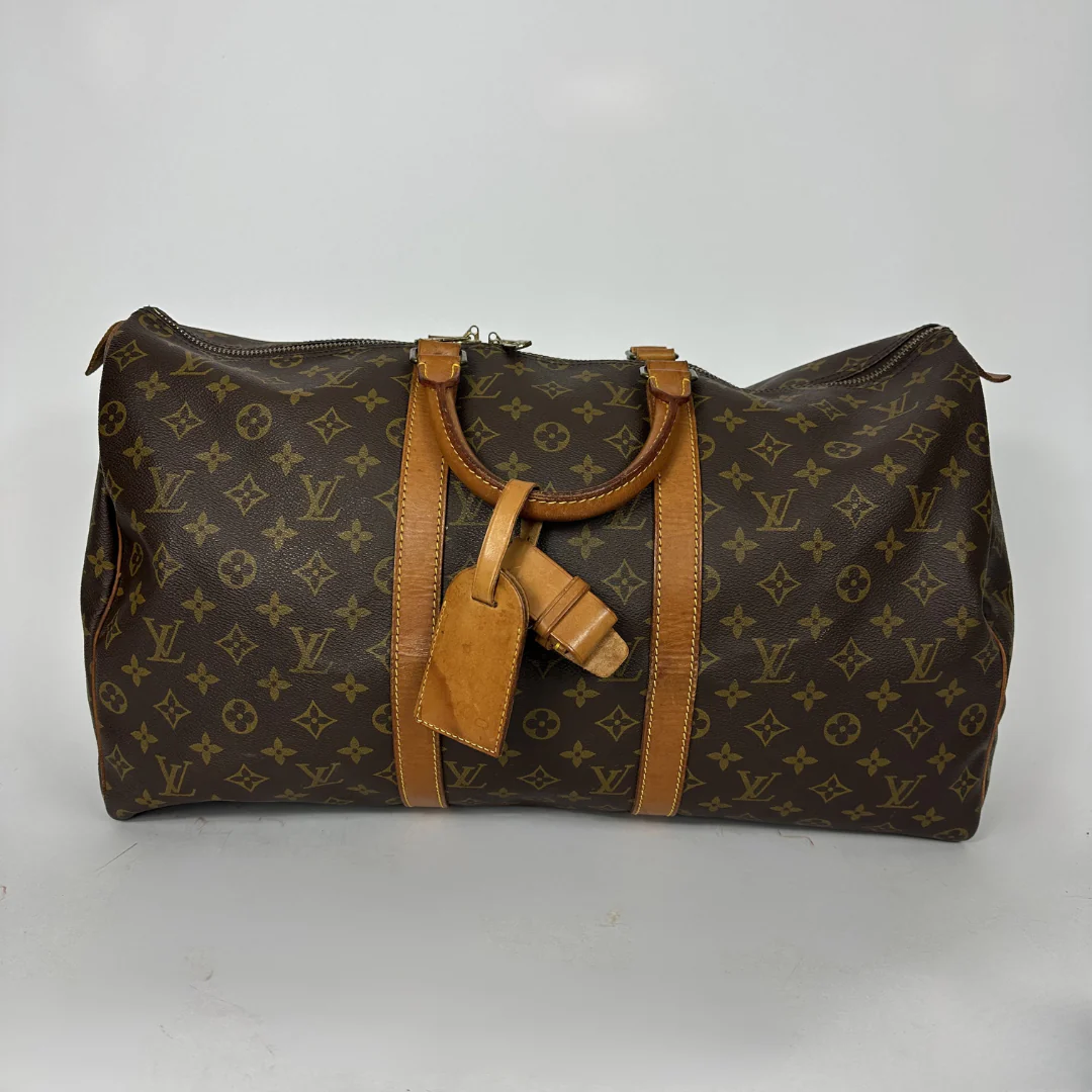 Brown monogram patterned duffel bag with tan leather straps on a white background