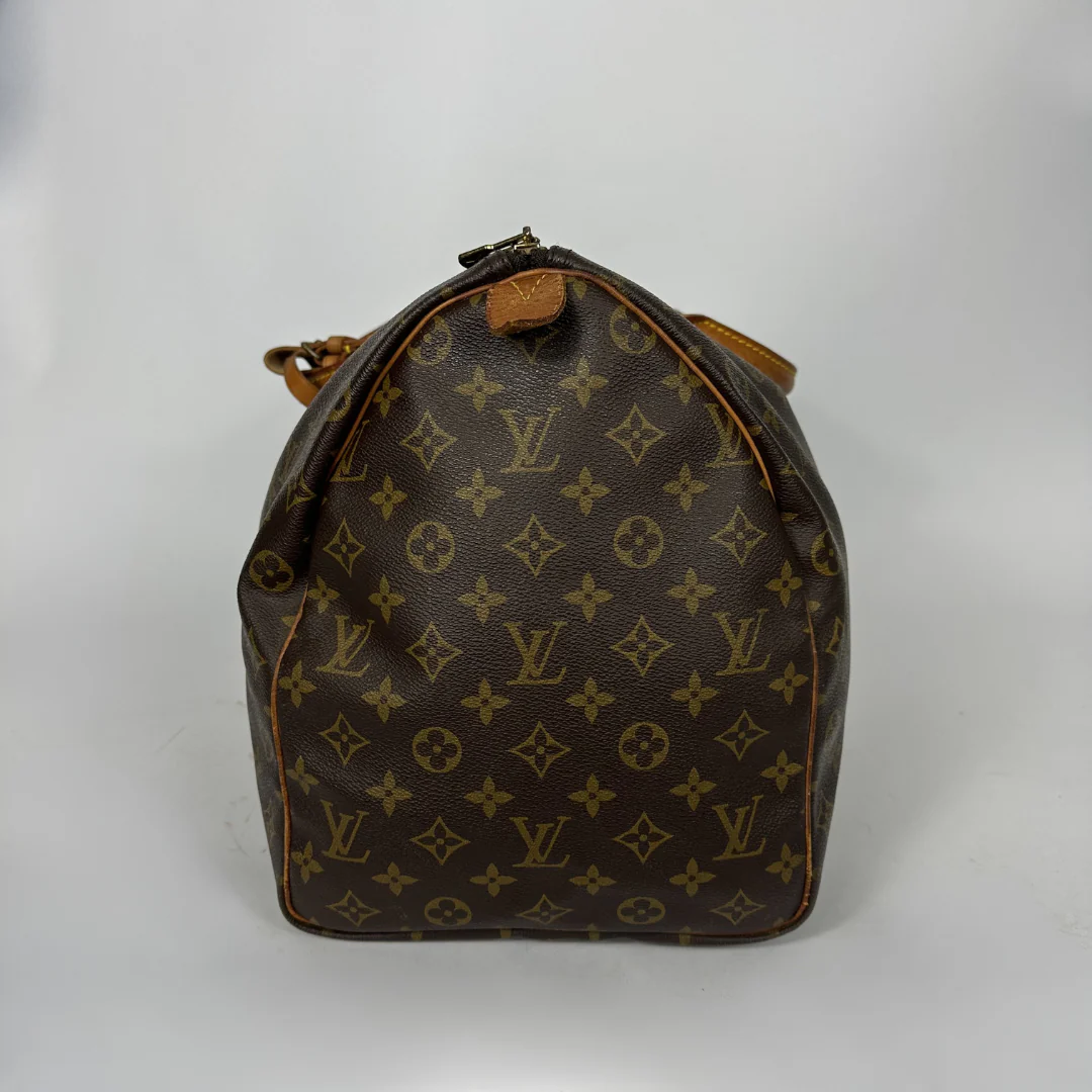Brown monogram patterned duffel bag with tan leather straps on a white background