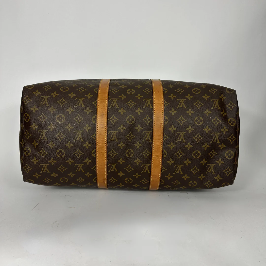 Brown monogram patterned duffel bag with tan leather straps on a white background