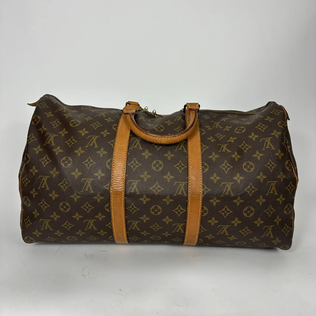 Brown monogram patterned duffel bag with tan leather straps on a white background