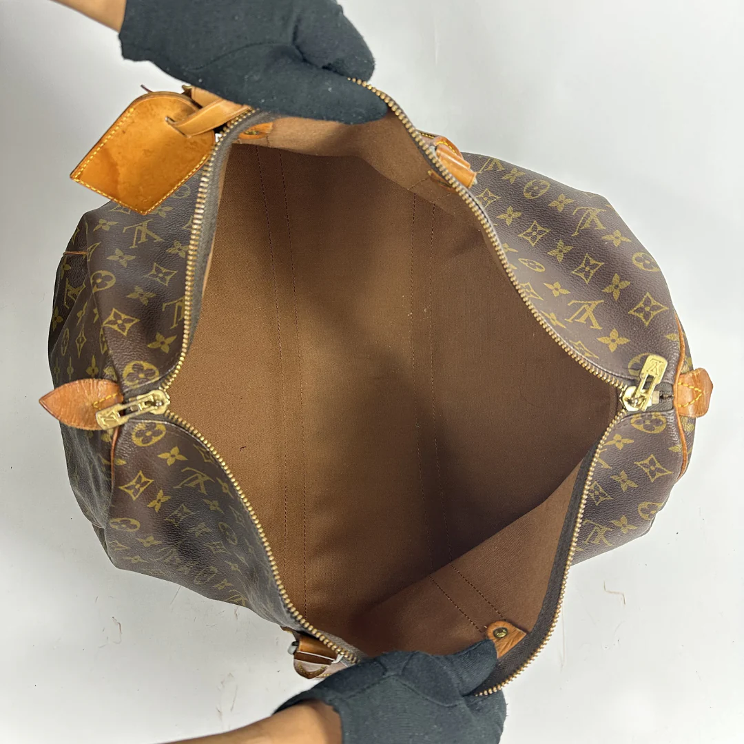 Brown monogram patterned duffel bag with tan leather straps on a white background