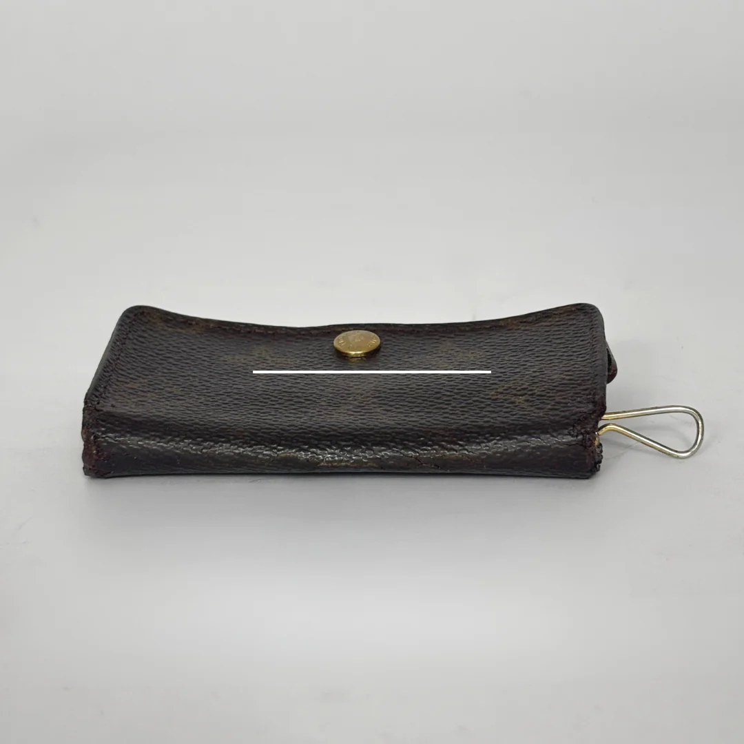 Black leather key case with a gold button and keychain on a light gray background