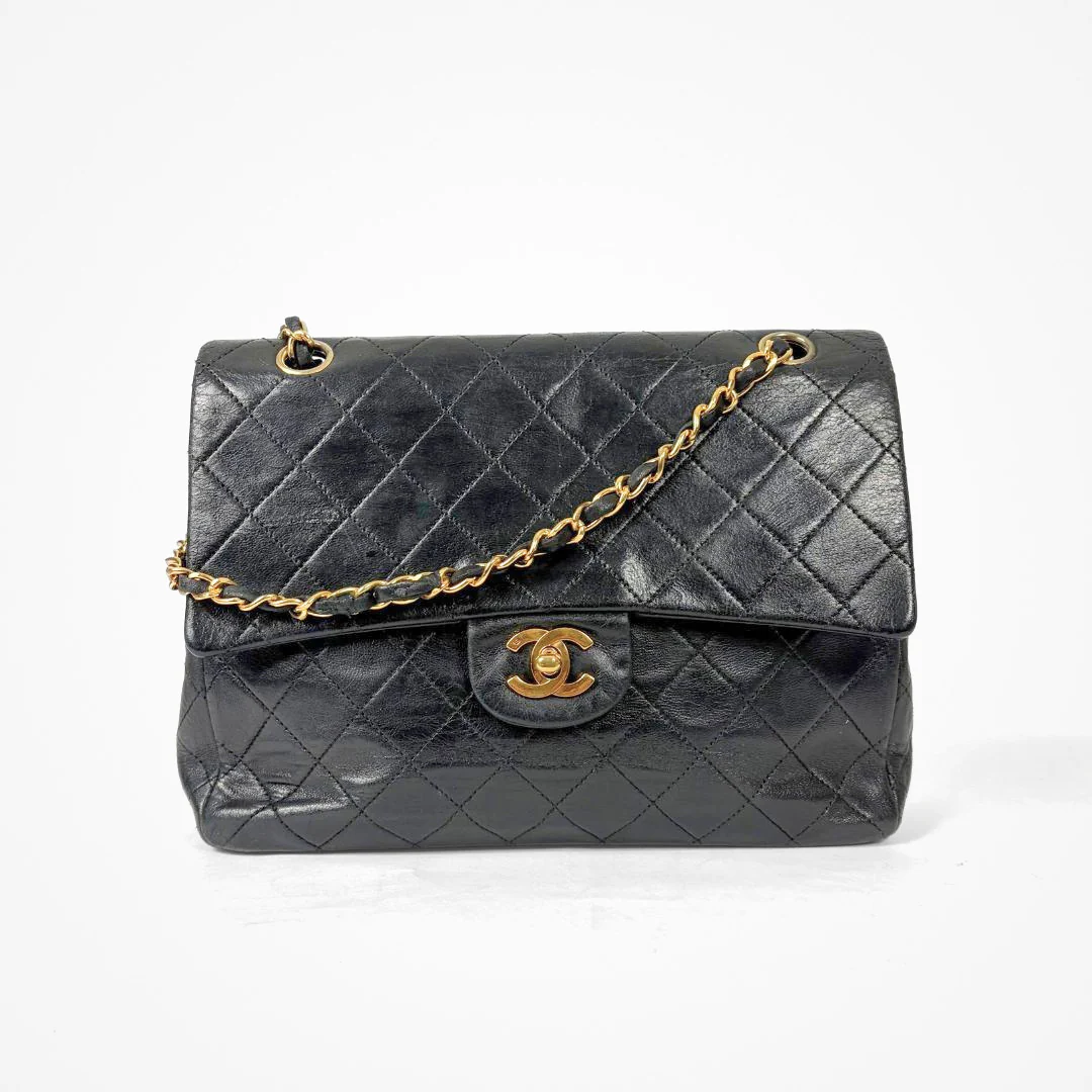 Black Chanel handbag with gold chain and clasp on a white background
