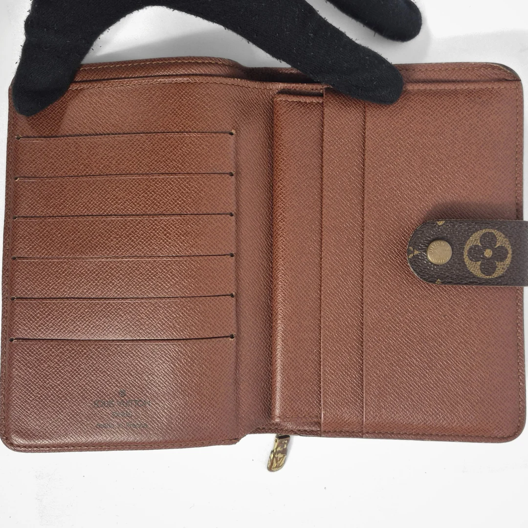 Brown wallet with a gold zipper and brand logo, held open by a black glove.