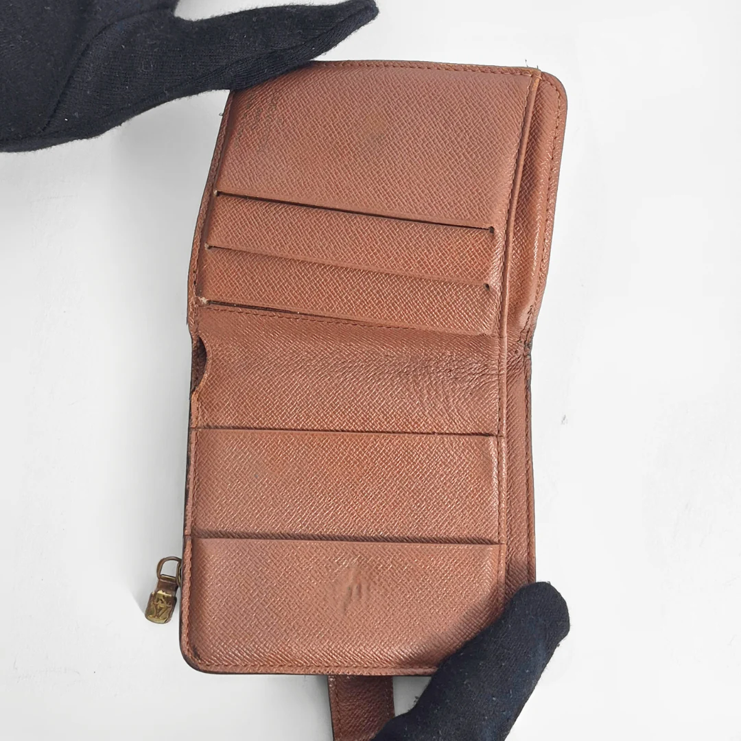 Brown leather wallet held by a gloved hand on a white background