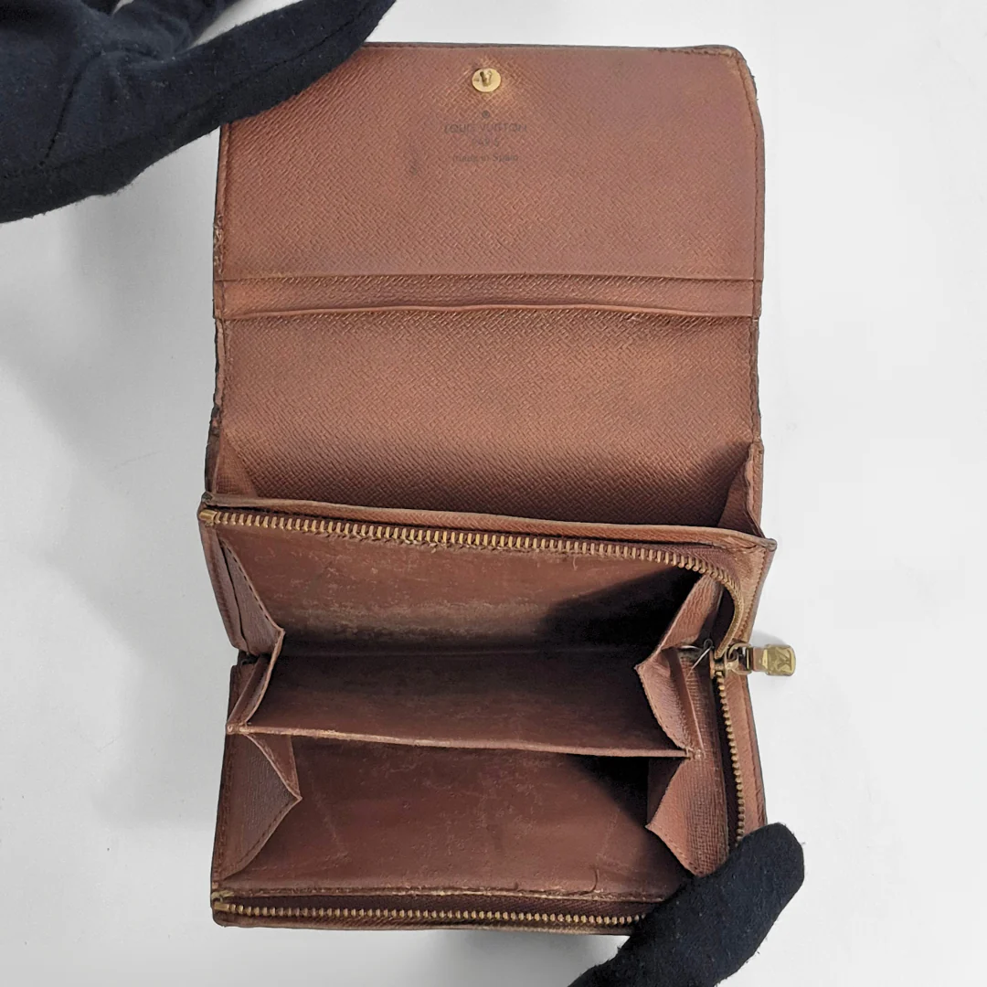Brown leather wallet with gold zipper held by a gloved hand on a white background