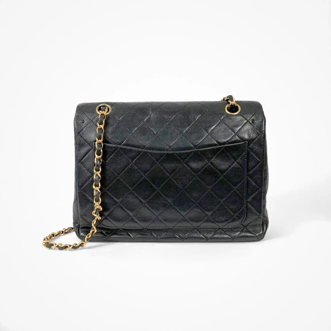 Black Chanel handbag with gold chain and clasp on a white background