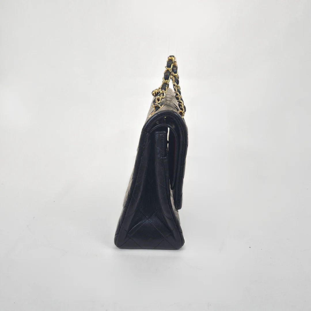 Black Chanel handbag with gold chain handle and clasp on a white background