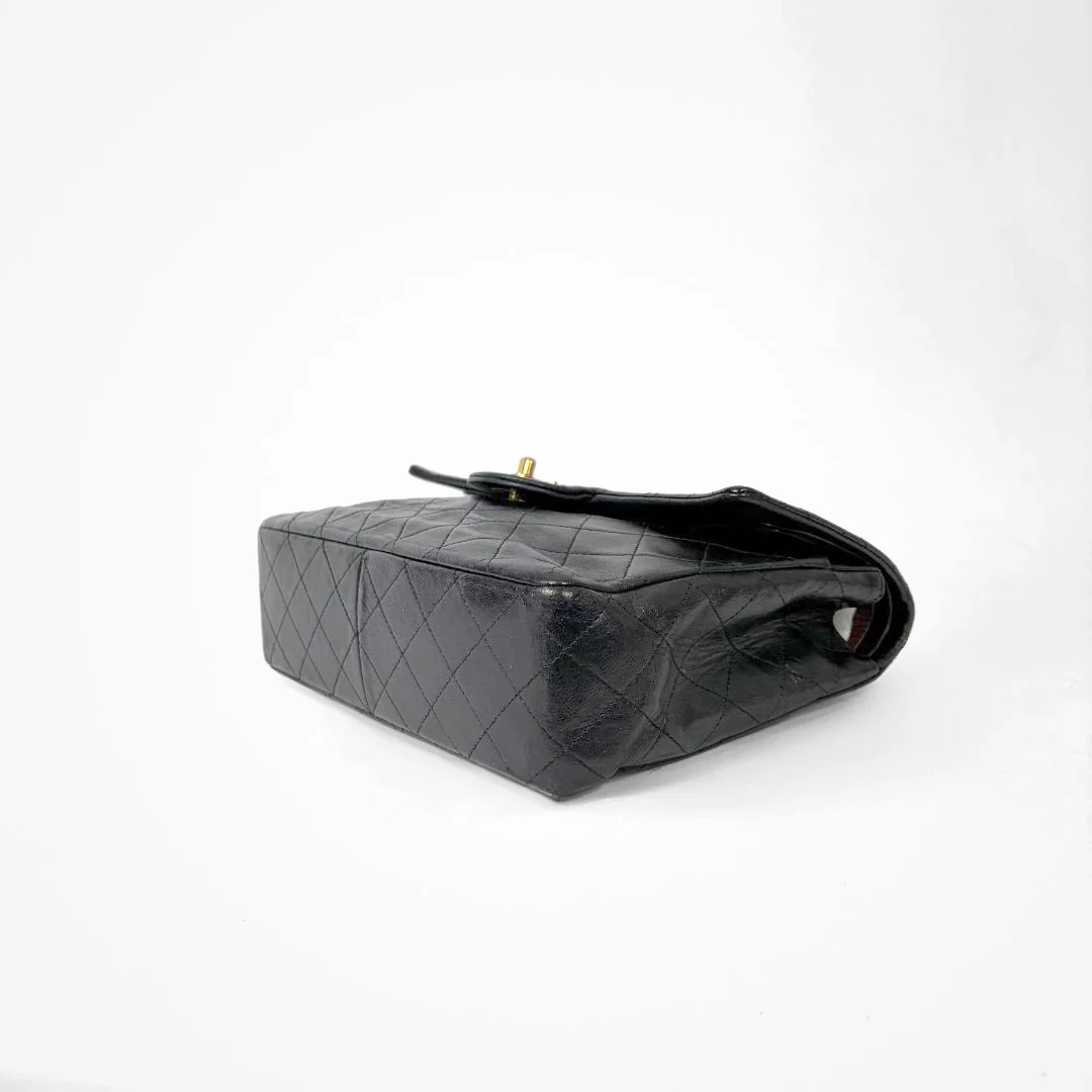Black Chanel handbag with gold chain and clasp on a white background