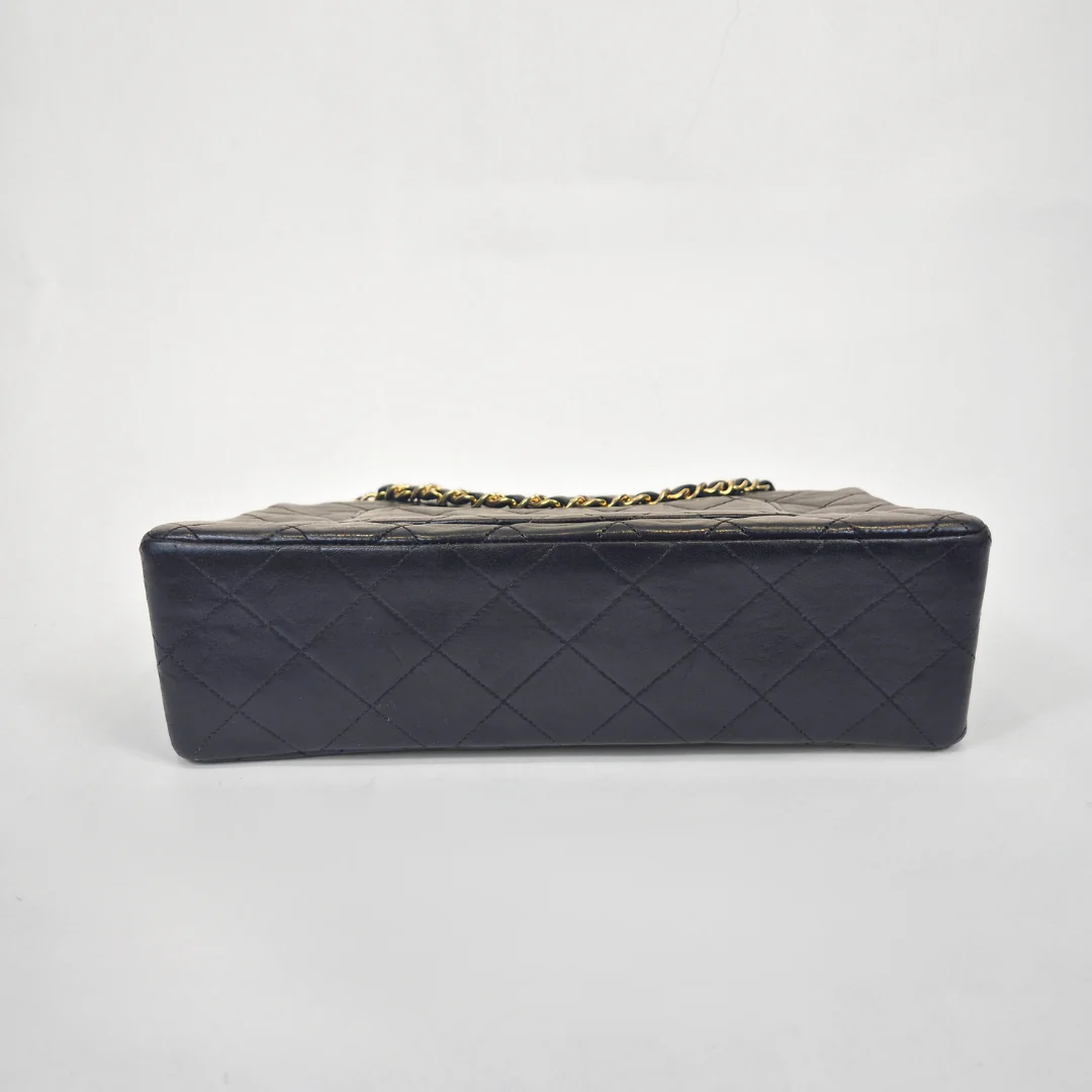 Black Chanel handbag with gold chain handle and clasp on a white background