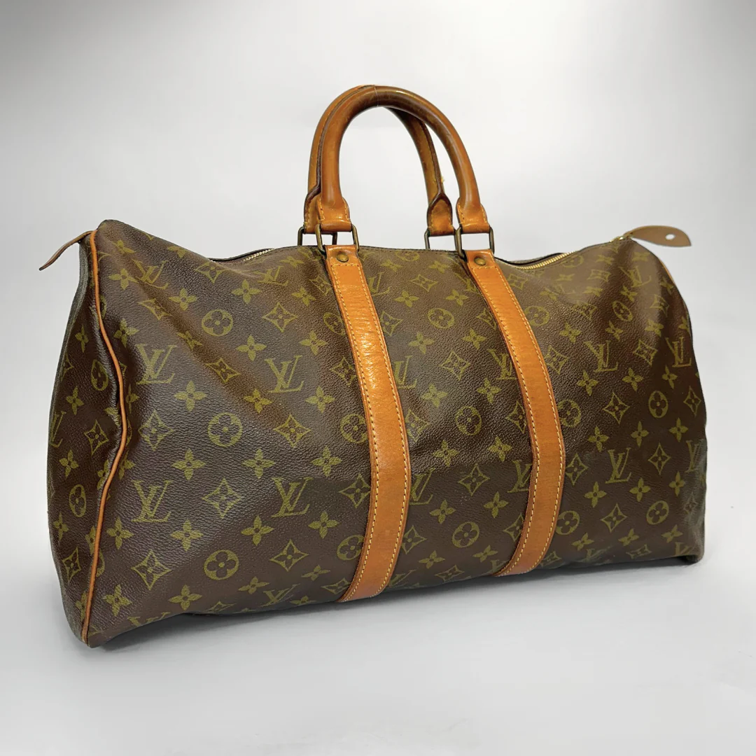 Brown monogrammed travel bag with tan leather handles and straps on a white background