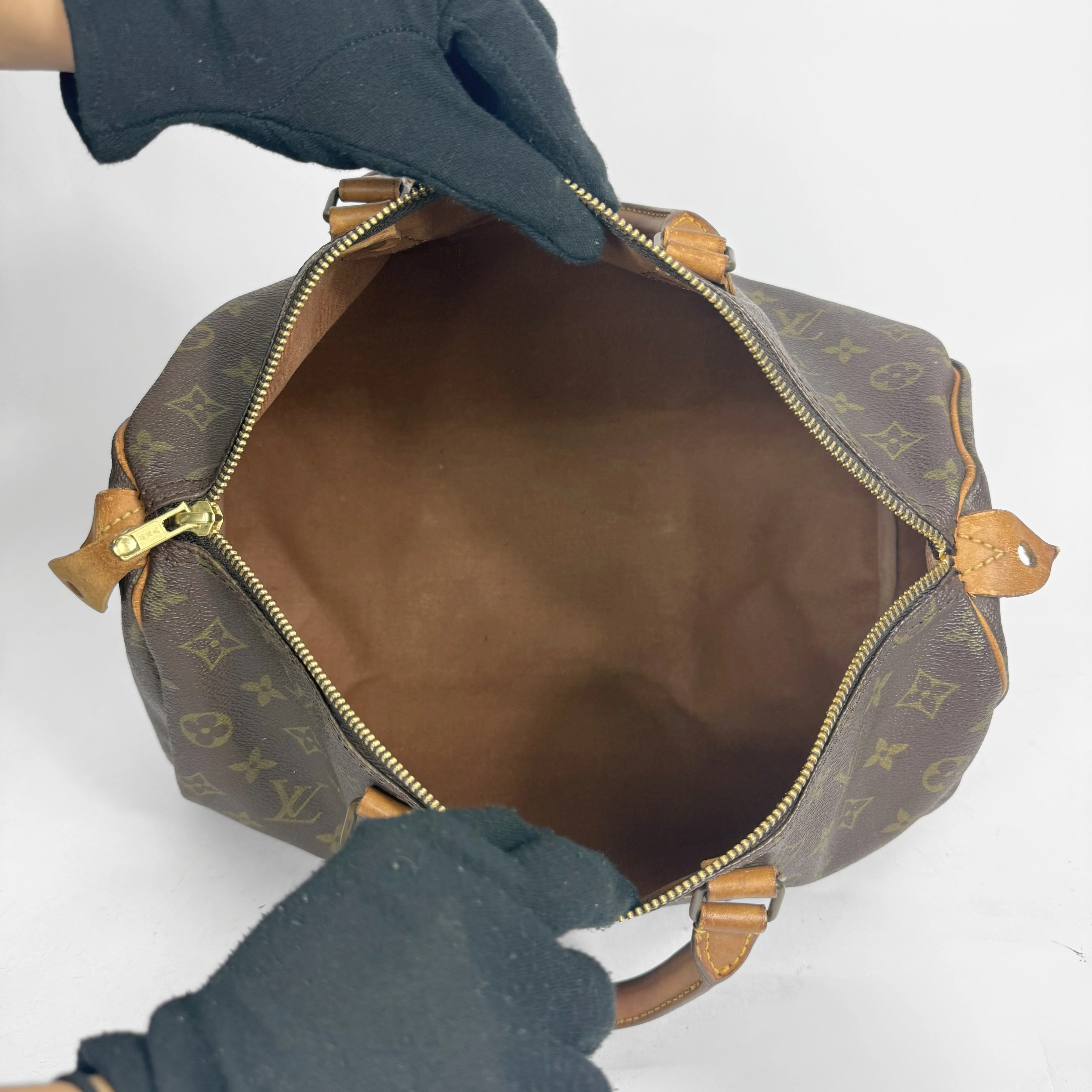 Brown Louis Vuitton bag with gold monogram pattern held open by gloved hands on a white background