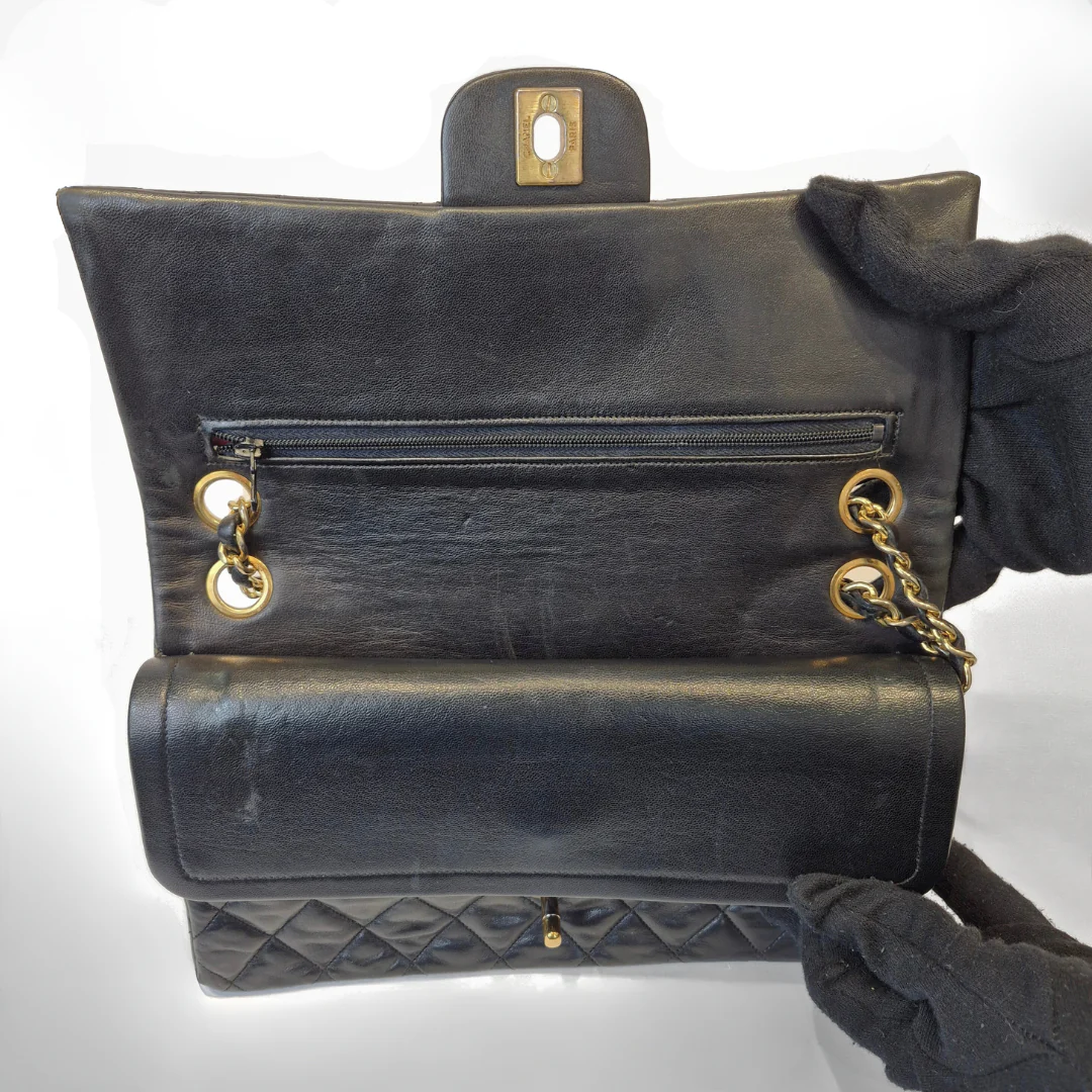 Black Chanel handbag with gold chain handle and clasp on a white background