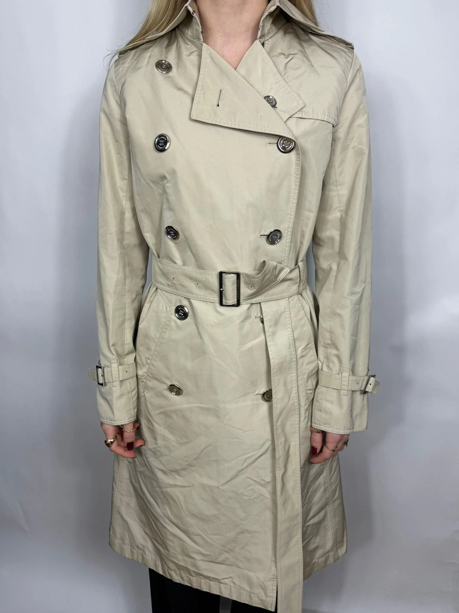 Beige trench coat worn by a person on a white background